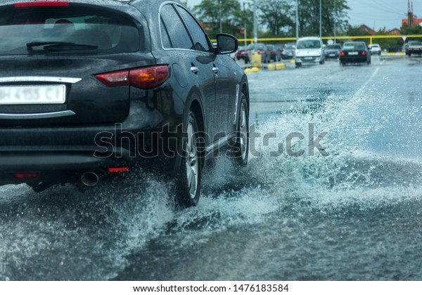 driving car on flooded road\
during flood caused by torrential rains. Cars float on water,\
flooding streets. Splash on the car. Flooded city road with a large\
puddle