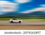 Driving car on speed blurred background. A sporty white SUV is driving on the highway, with blurred clouds and mountains in the background. Car with free space for text, copy space.