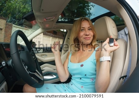 Driving a car. Pretty young woman in dress and sunglasses driving her modern car in the city. Blonde, long hair. She is happy in summer day