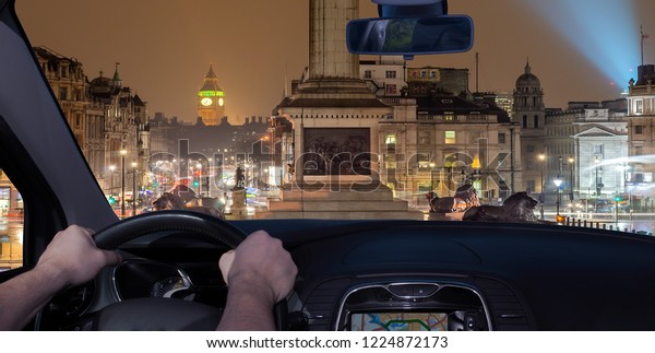 Driving a car in Trafalgar Square\
at night with the Big Ben on the background, London,\
UK