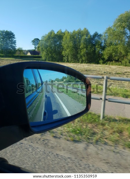 Driving in car, view\
through mirror to road. Reflecting highway on car mirror. Road trip\
with vehicle, machine. Travelling through different nature\'s\
landscape. 