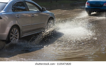 Driving cars on a flooded road during floods caused by rain storms. Cars float on water, flooding streets. Splash on the machine. Flooded city road with a big puddle - Shutterstock ID 1135471820