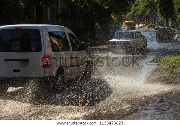 Driving cars on a flooded\
road during floods caused by rain storms. Cars float on water,\
flooding streets. Splash on the machine. Flooded city road with a\
big puddle
