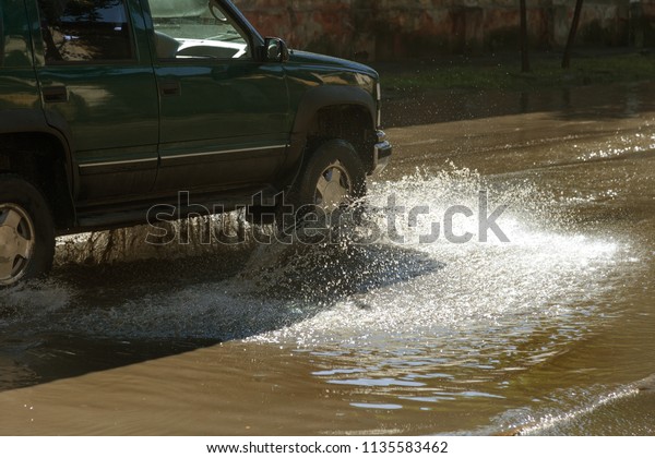 Driving cars on a flooded\
road during floods caused by rain storms. Cars float on water,\
flooding streets. Splash on the machine. Flooded city road with a\
big puddle