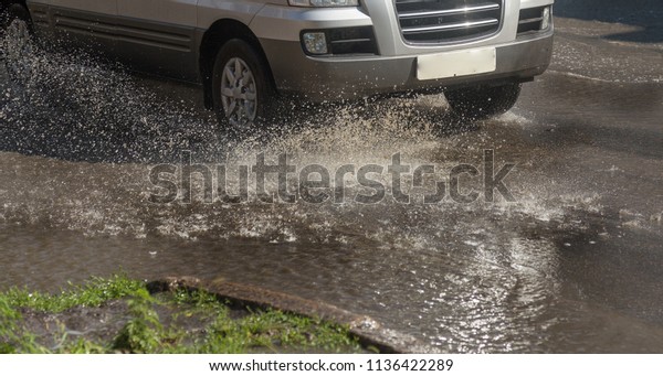 Driving cars on a flooded
road during floods caused by rain storms. Cars float on water,
flooding streets. Splash on the machine. Flooded city road with a
big puddle