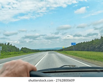 Driving down an open road with a view of fields under a cloudy sky, showing freedom and the spirit of travel in summer.