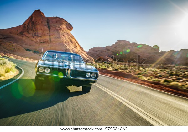 driving fast through desert in vintage hot\
rod car with lens flare and motion\
blur