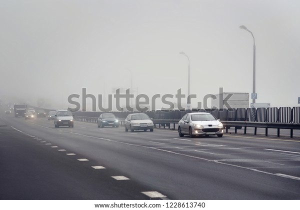 Driving in the fog and mist. Bad driving conditions\
in haze. Dangerous situation on the road. Foggy gray road, cars and\
trucks driving fading into the thick fog. Low visibility. Smoke on\
the road.