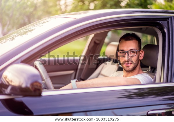 Driving with glasses. Young urban and handsome\
man with glasses in car driving\
