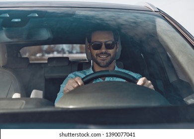 Driving his brand new car. Handsome young man smiling while driving a status car