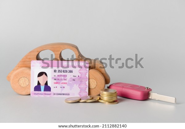 Driving license with key, coins and wooden car\
on light background