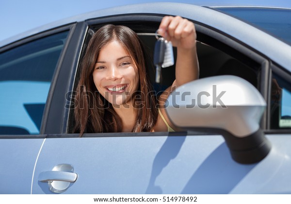 Driving new\
rental car or drivers license concept. Young teenager woman driver\
holding car key driving her new car. Beautiful multiracial Asian\
woman smiling showing new car\
keys.