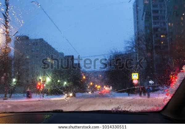 driving in night\
snowfall in Moscow - unfocused background with view of street in\
Moscow city in snowy evening through wet windscreen (focus on\
melting trickle on car\
glass)