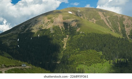 Driving an off road car on a gravel road near a mountain peak along an abyss. Clouds are casting their shadows on Balota peak. Carpathia, Romania. - Powered by Shutterstock