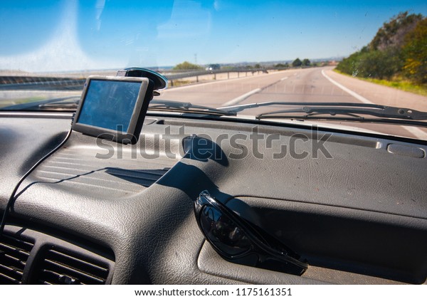 Driving an old car with poor interior on a road.\
GPS system on windshield, and sunglasses in the car. Summer\
travelling concept in Eastern\
Europe.