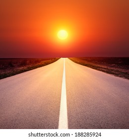 Driving on an empty asphalt road towards the setting sun