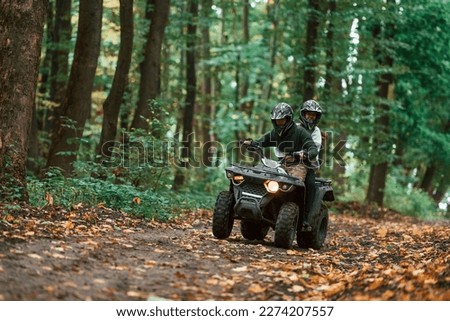 Driving on the footpath. Young couple riding a quad bike in the forest.