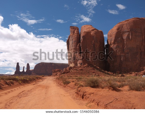 Driving on Loop Road in\
Monument Valley, Three sisters, Camel Butte and The Thumb rock\
formations, car