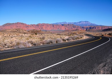 Driving On The Smooth, Black Pavement Of Old Highway 91 In South Western Utah. On The Horizon Is Red Rock Country Under Cloudless, Blue Skies