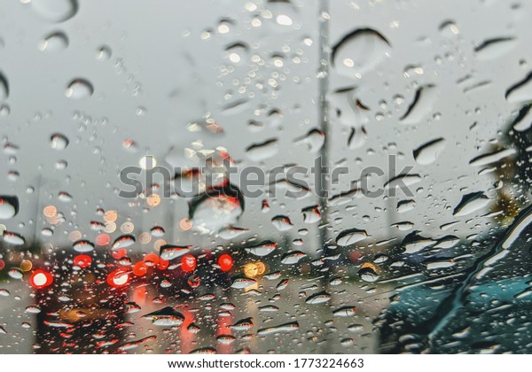 Driving in rain. Rain drop\
on the car glass background. Abstract traffic in raining day. View\
from car seat. Road view through car window with rain drops,\
selective focus. 
