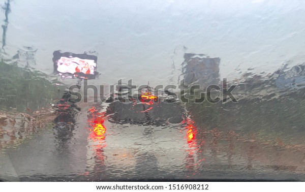 Driving in the\
rain, sight through a watery front windshield. Car red lights and\
motorcycle. Drive safe\
concept.