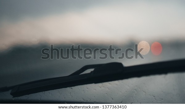 Driving in rain weather. Blur Background with\
bokeh. Car window with drops of rain in rainy day. View from car\
seat. Blurred droplet on car window, sun light over empty road.Car\
wiper glass raindrops.
