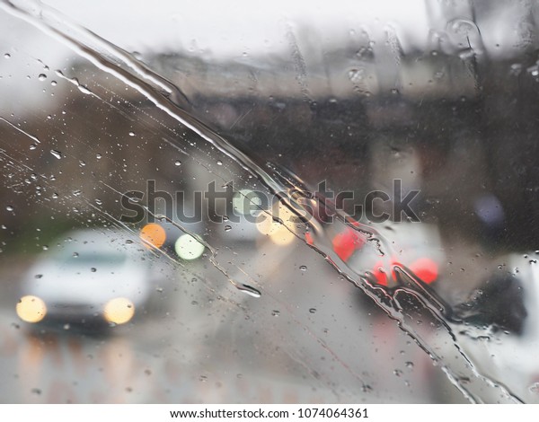 Driving in rain. Windshield wipers\
from inside of car, rain drops. City street, traffic\
jam