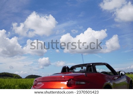 Driving in a red open car through the countryside and the blue sky with clouds floating in it