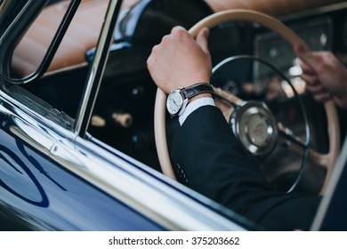 driving a retro car driver sitting in a suit and holding a steering wheel, the driver on the hand watch.