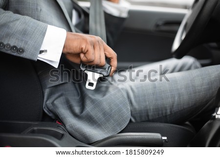 Driving safety concept. Unrecognizable black businessman fasten seat belt in his car, ready to go to office. African american man in stylish suit putting on his seatbelt before driving car, cropped