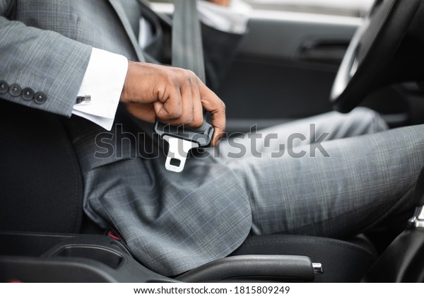 Driving safety concept. Unrecognizable black\
businessman fasten seat belt in his car, ready to go to office.\
African american man in stylish suit putting on his seatbelt before\
driving car, cropped