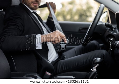 Driving safety concept. Unrecognizable businessman fasten seat belt in his car, ready to go to office. Man in stylish suit putting on his seatbelt before driving car to airport, cropped
