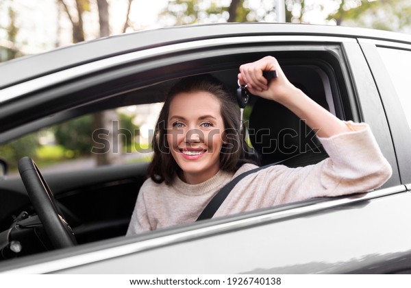driving, safety and people concept -\
young woman or female driver sitting in car and showing\
key