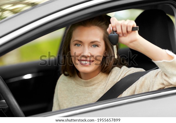 driving, safety and people concept -\
young woman or female driver sitting in car and showing\
key