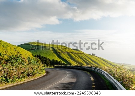 Driving scenic winding road on a sunny day through valley and green hills. Empty asphalt road leading into distance