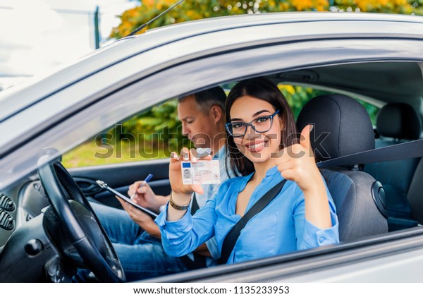 Driving school. Beautiful young woman successfully\
passed driving school test. She looking sitting in car, looking at\
camera and holding driving license in hand. Girl with driving\
license 