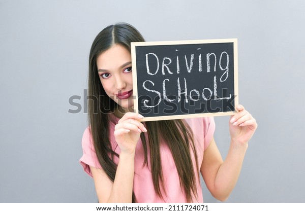Driving school idea and concept, student driver\
passed the exam, drivers license, portrait of a beautiful happy\
young woman. on a gray isolated background. plate with the\
inscription Driving\
school