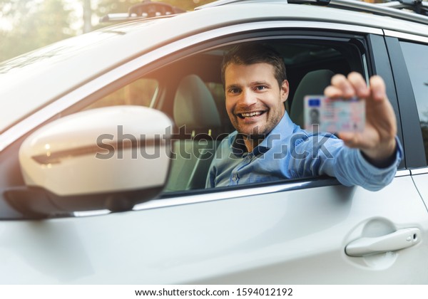 driving school - man sitting in the car and\
showing his driver license out of car\
window