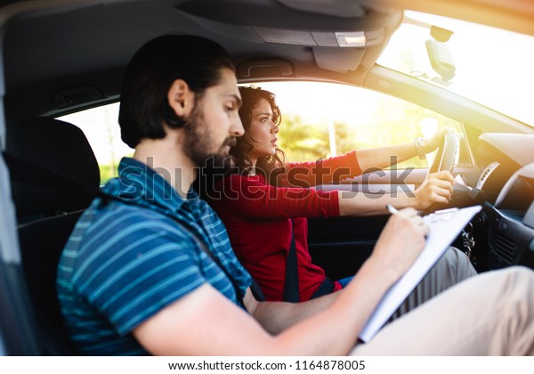 Driving school or test.\
Beautiful young woman learning how to drive car together with her\
instructor