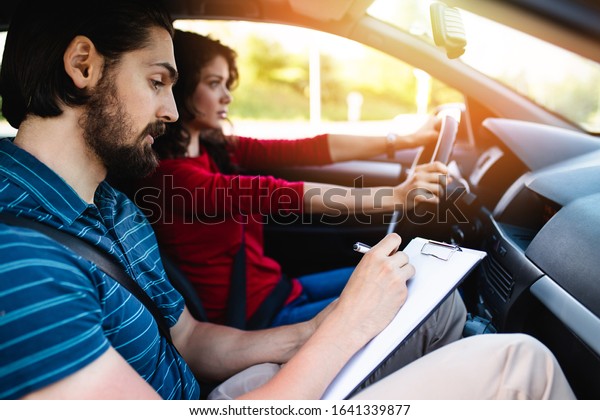 Driving school or test.\
Beautiful young woman learning how to drive car together with her\
instructor. 