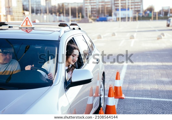 Driving\
school or test. Beautiful young woman with male instructor learning\
how to drive and parking car between\
cones.