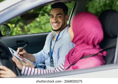 Driving School Test. Handsome Young Arab Instructor Examining Muslim Female Driver, Islamic Lady In Hijab Holding Steering Wheel, Sitting In Car Next To Teacher, Successfully Passed Drive Exam