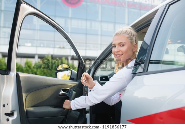 Driving school. Young happy woman getting out of the\
car. Driver student proudly showing the key. Free space for text.\
Copy space. 