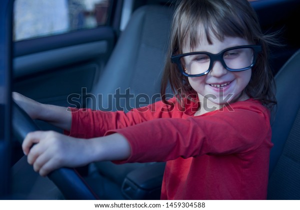 Driving shool. Humorous photo of happy cute little\
child girl learns to\
drive.