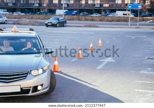 Driving Test. Training\
parking. Cones for the examination, driving school concept. Alert\
young woman student driver taking driving education lesson test\
from male instructor.