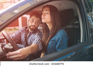 Driving test. Young serious woman driving car feeling inexperienced, looking nervous at the road traffic for information to make appropriate decisions. Man is an instructor, controlling and checking