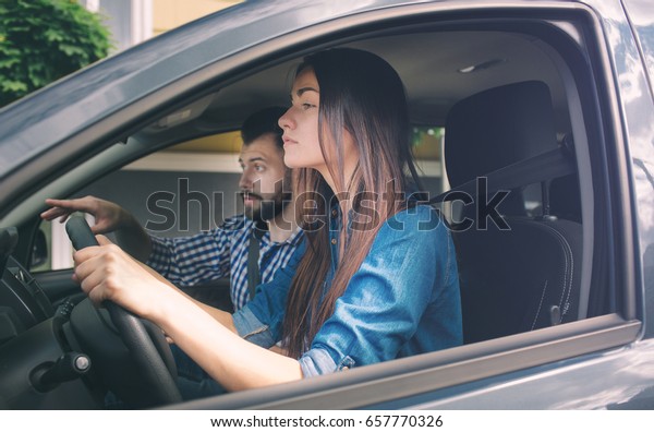 Driving test. Young serious woman driving car\
feeling inexperienced, looking nervous at the road traffic for\
information to make appropriate decisions. Man is an instructor,\
controlling and\
checking