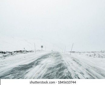 Driving through blizzard snowstorm on black ice and snowy white road and landscape in Norway.