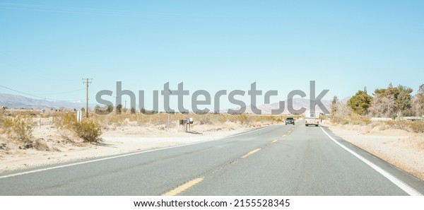 Driving through the\
colorado desert. Cars in the distance of a big road. Sand, scrub,\
bushes, trees and telephone poles on the side. Mountains rise up in\
the distance. 