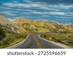 Driving through the dramatic, multi-hued badlands landscape. Curved highway under a striking sky, representing freedom, adventure, and the ultimate road trip.